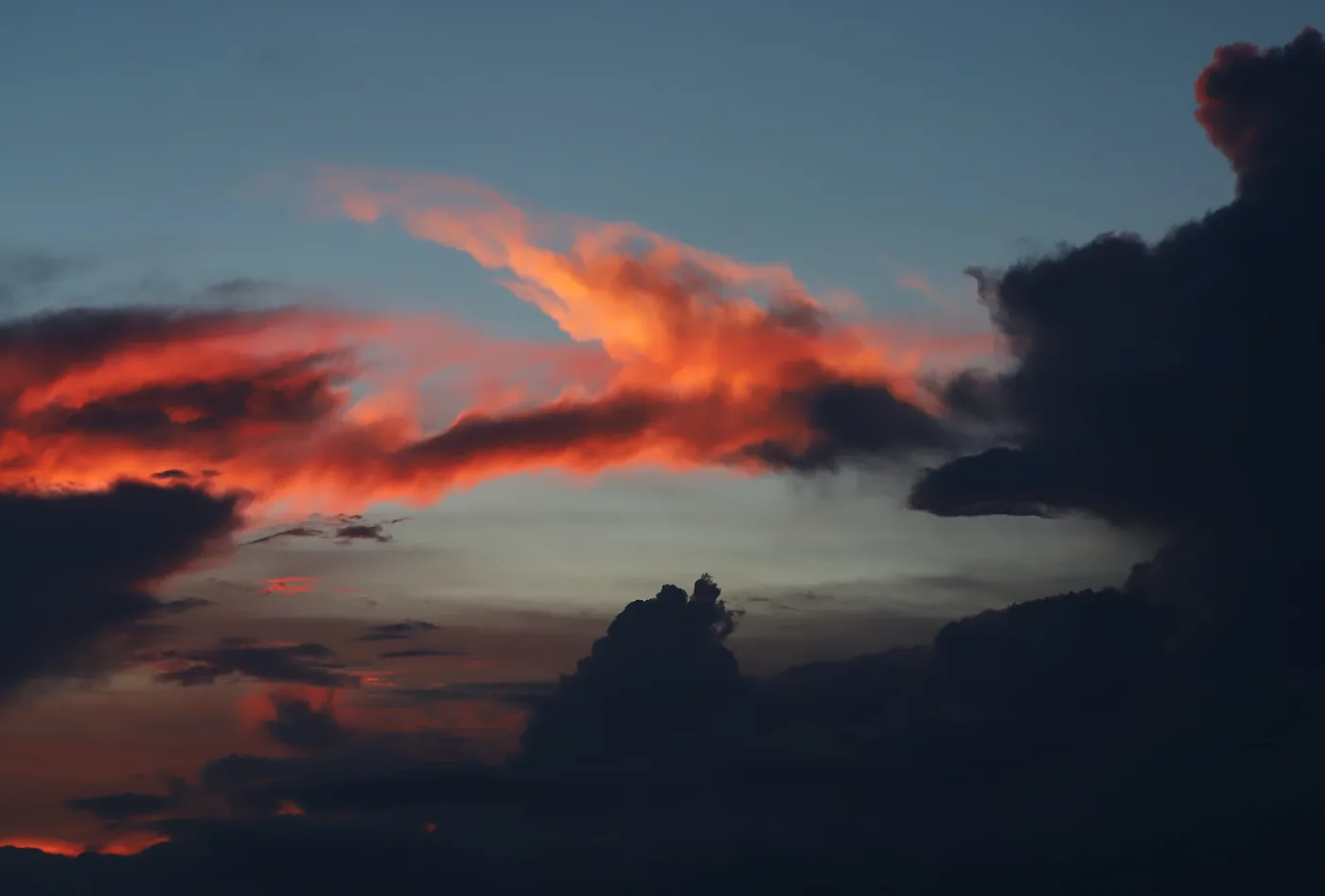 A streak of fiery cloud lit red against the deep blue of a fading sky.