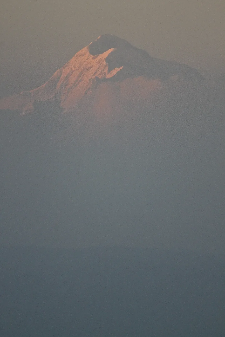 A snow peak catching the first pink light, half-dissolved in heavy dawn haze.