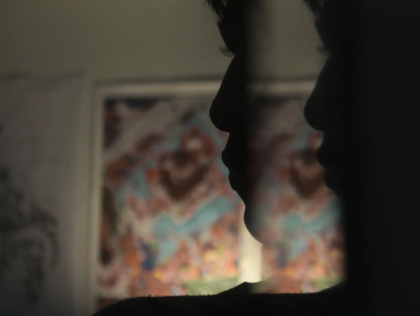 The silhouetted profile of a face against a soft, blurred picture on the wall.