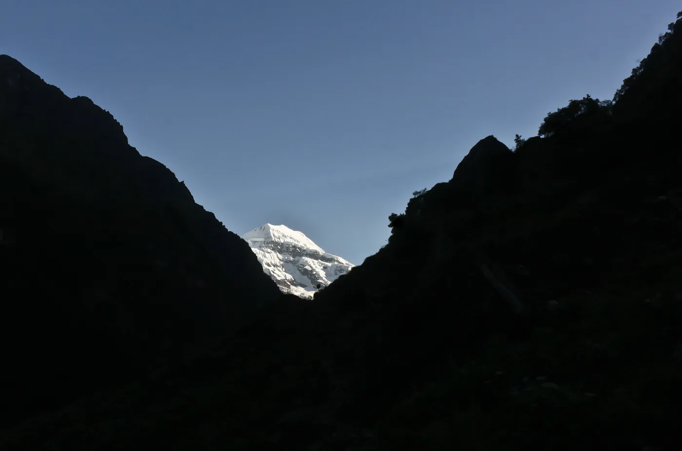 A sunlit snow peak framed in the dark V between two silhouetted ridges.