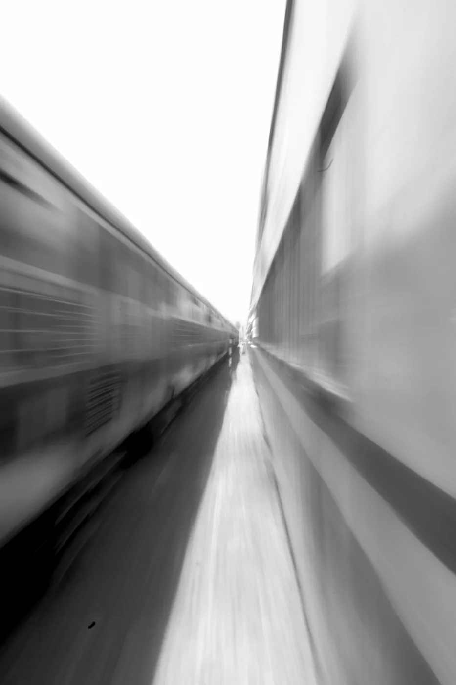 A blurred rush of motion between two passing trains, reduced to streaks of grey and white.