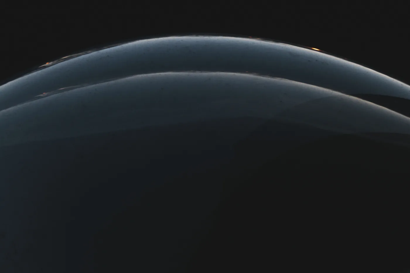 Faint curved arcs of pale light bending across a black field.
