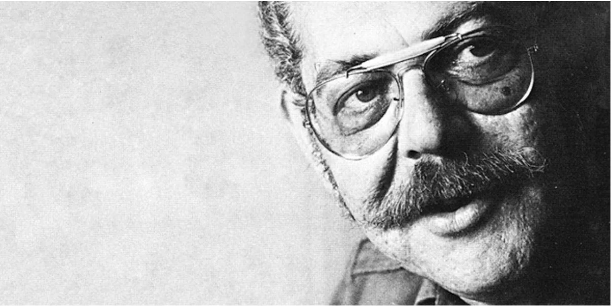 Black-and-white portrait of Victor Papanek in aviator glasses, moustached, looking past the camera.