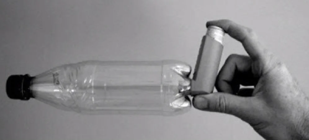A hand fits a small inhaler canister into the dimpled base of a clear plastic bottle.