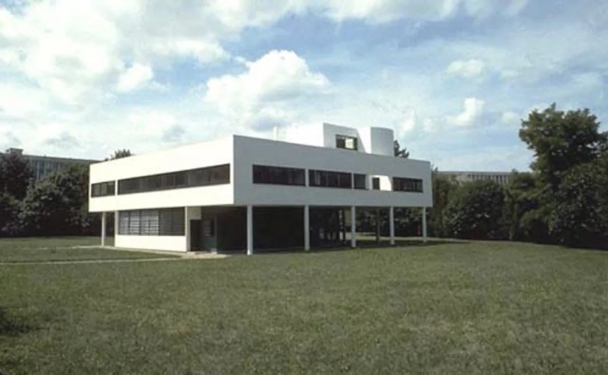 Villa Savoye: a white box on slender pilotis with ribbon windows, standing on a lawn beneath a cloudy sky.