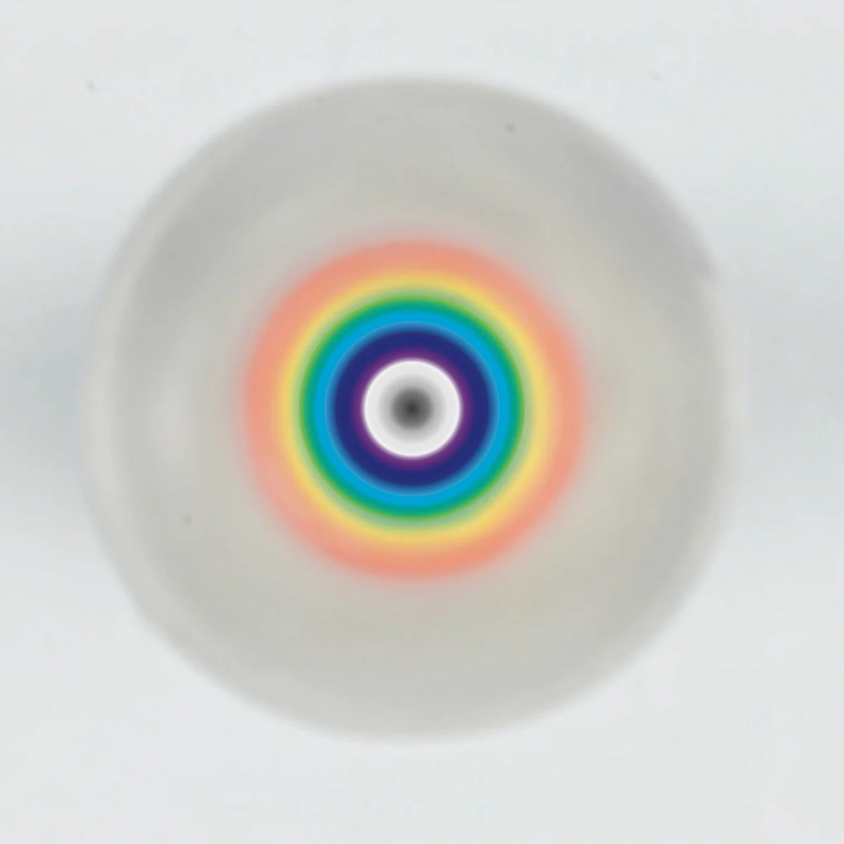 Photograph looking straight down the axis of the acrylic cone: the painted spectrum reads as concentric rings, red and orange at the rim passing through yellow, green and blue to deep violet, around a white centre with a small dark core.